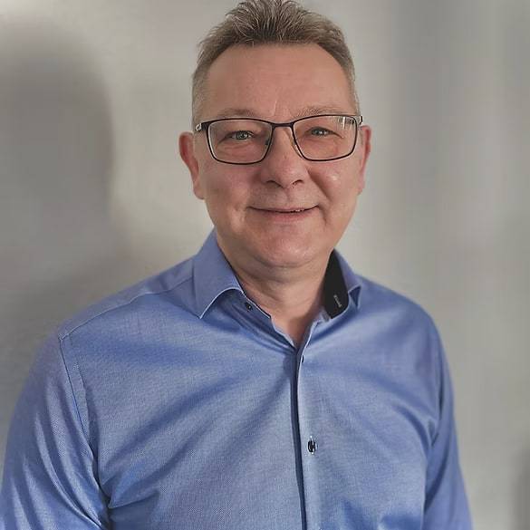 Porträt eines Mannes mit Brille und hellblauem Hemd vor einer hellen Wand