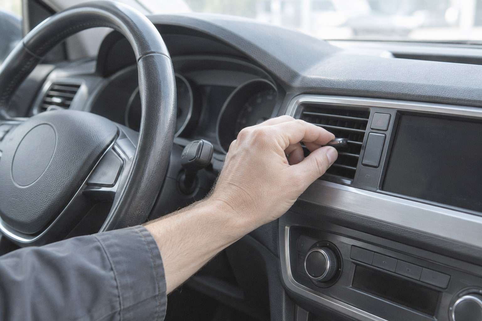 Eine Hand stellt am Armaturenbrett eines Fahrzeugs eine Lüftungsdüse ein