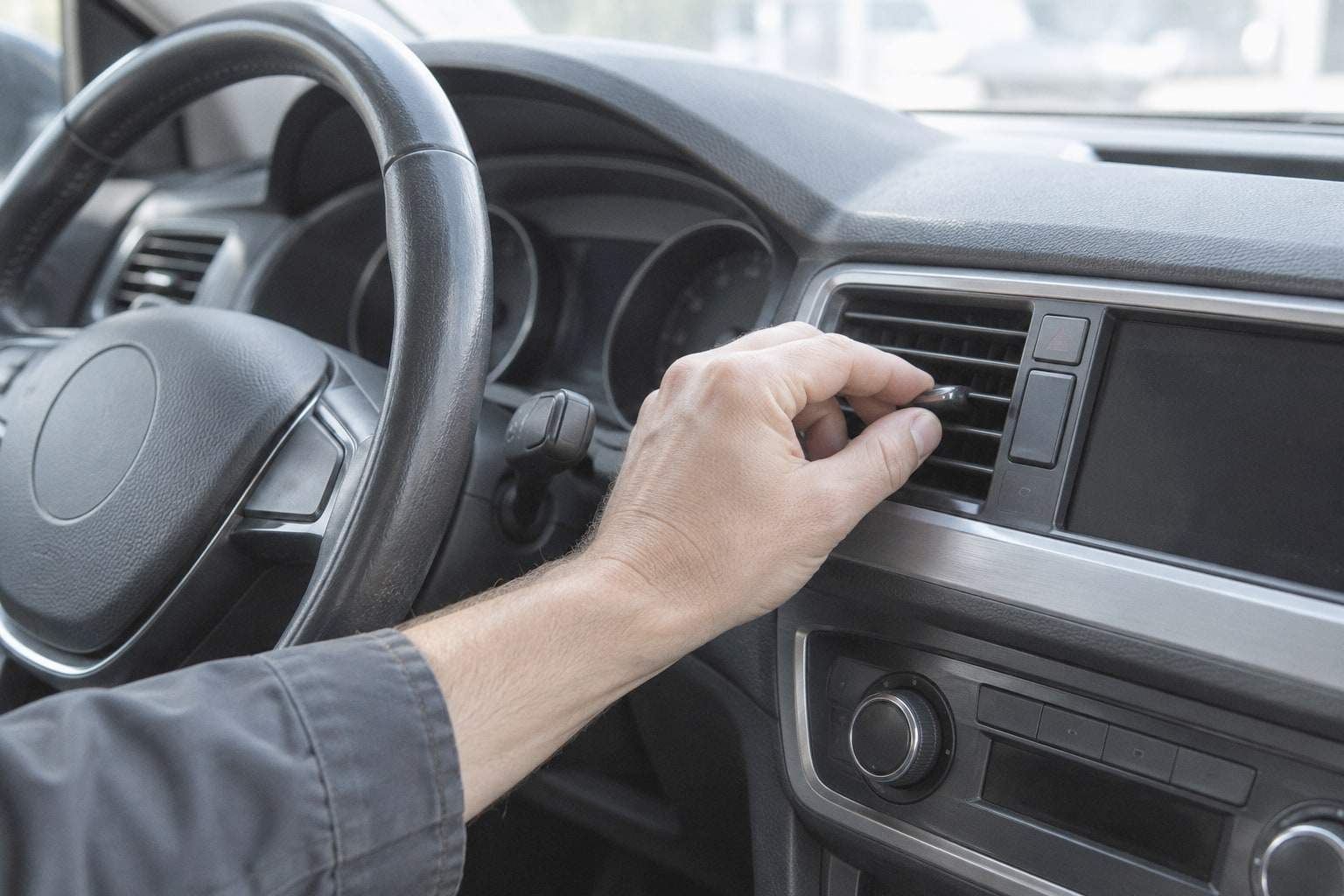 Eine Hand stellt am Armaturenbrett eines Fahrzeugs eine Lüftungsdüse ein